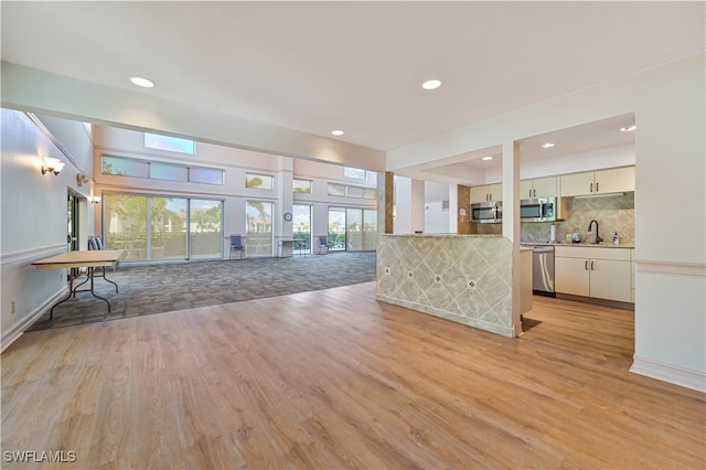 kitchen with sink, decorative backsplash, stainless steel appliances, and light wood-type flooring