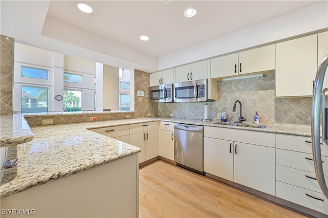 kitchen featuring appliances with stainless steel finishes, sink, light wood-type flooring, kitchen peninsula, and light stone counters