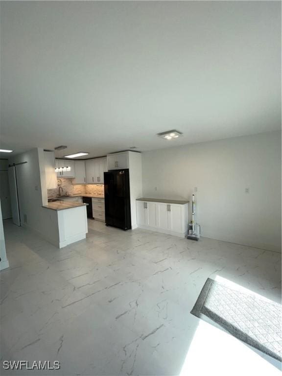 kitchen featuring decorative backsplash, white cabinetry, black refrigerator, and sink