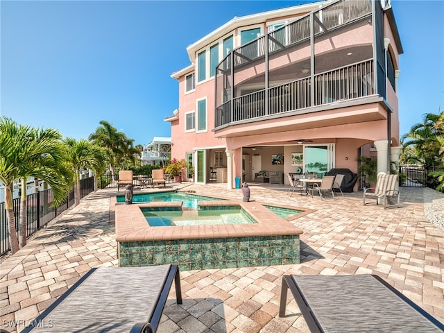 rear view of property featuring a swimming pool with hot tub, a balcony, ceiling fan, and a patio area