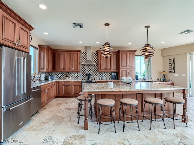 kitchen featuring appliances with stainless steel finishes, a center island, decorative light fixtures, and wall chimney range hood