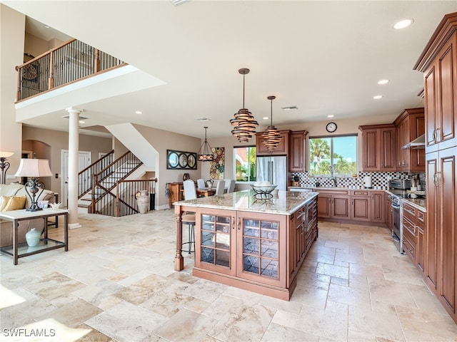 kitchen featuring a kitchen bar, appliances with stainless steel finishes, decorative columns, light stone counters, and a center island