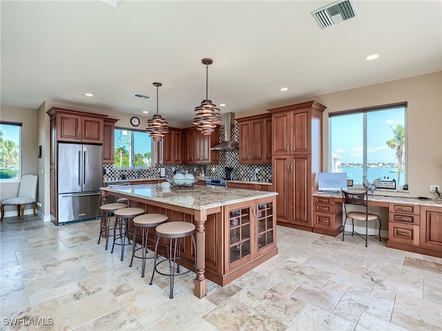 kitchen featuring wall chimney exhaust hood, a center island, a healthy amount of sunlight, and appliances with stainless steel finishes