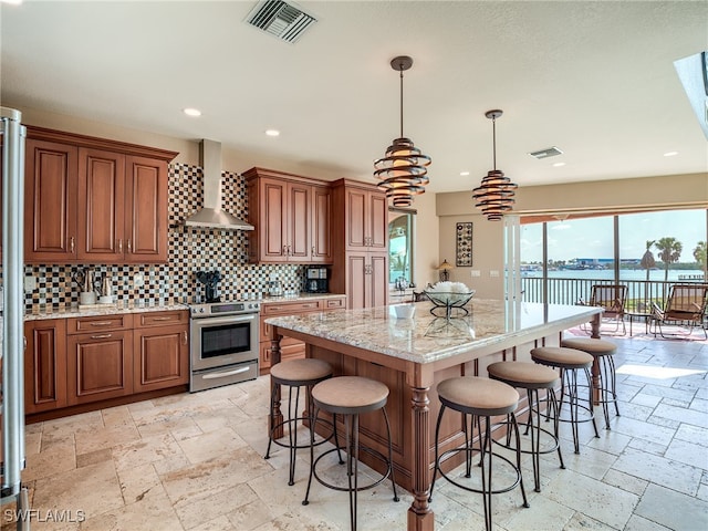 kitchen with a center island, stainless steel electric stove, a water view, wall chimney range hood, and decorative light fixtures