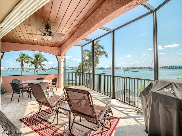 sunroom featuring ceiling fan, a water view, and wood ceiling