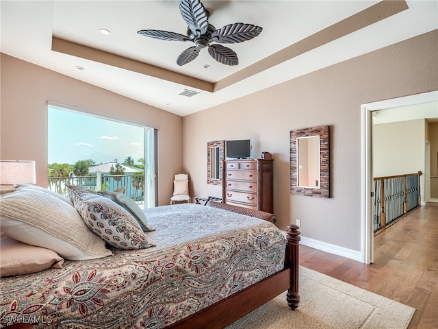 bedroom with a tray ceiling, access to exterior, ceiling fan, and light hardwood / wood-style flooring