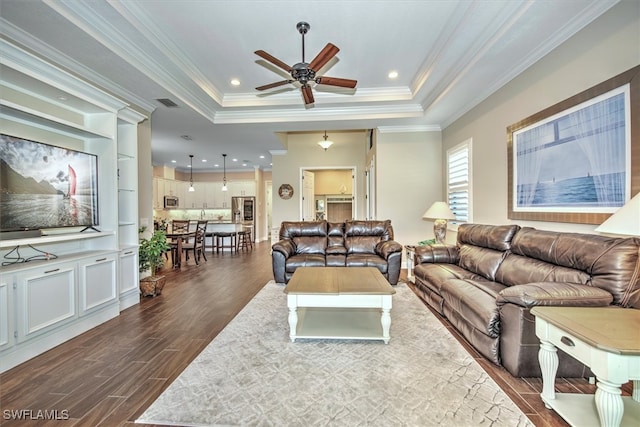 living room featuring crown molding, dark wood-type flooring, ceiling fan, and a tray ceiling