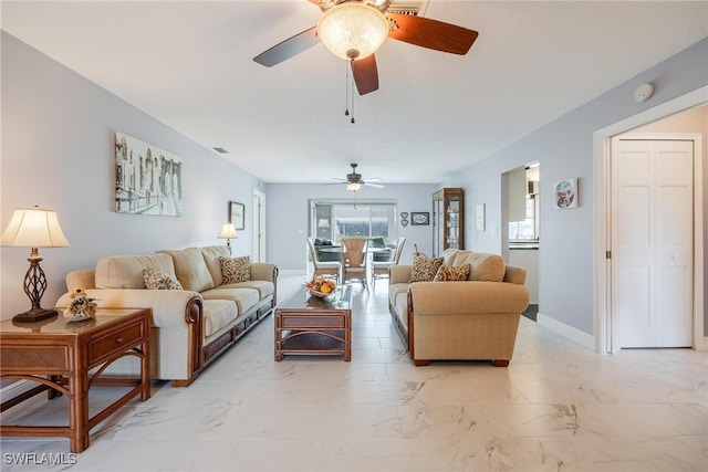 living area featuring a ceiling fan, marble finish floor, and baseboards