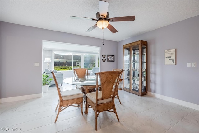 dining area with marble finish floor, a ceiling fan, baseboards, and a textured ceiling