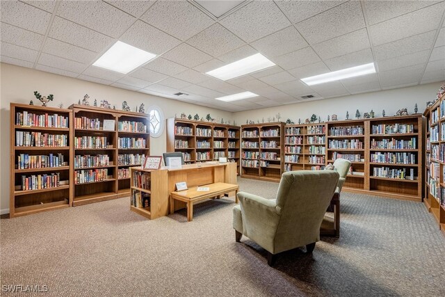 living area featuring carpet floors, a paneled ceiling, visible vents, and wall of books