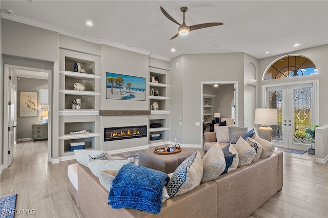 living room featuring ceiling fan, french doors, built in features, crown molding, and light wood-type flooring