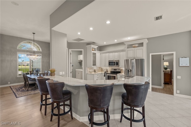 kitchen featuring a kitchen breakfast bar, white cabinetry, light wood-type flooring, and appliances with stainless steel finishes