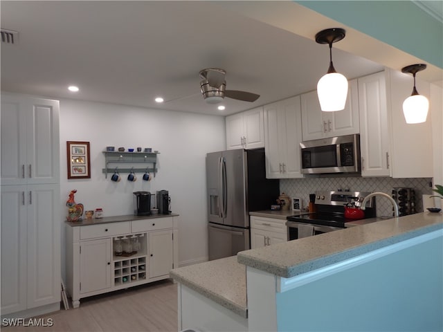 kitchen with tasteful backsplash, appliances with stainless steel finishes, kitchen peninsula, pendant lighting, and white cabinets