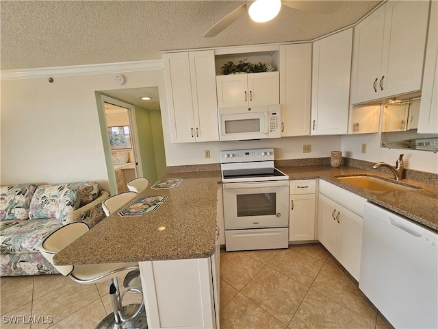 kitchen featuring sink, a breakfast bar area, a textured ceiling, white appliances, and white cabinets