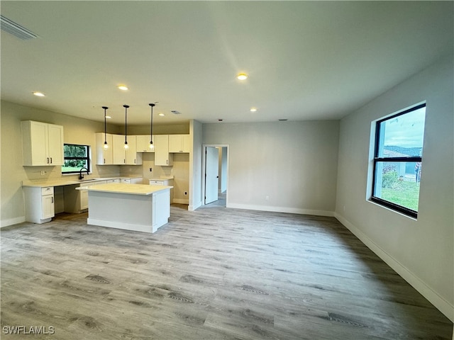 kitchen with white cabinets, sink, light wood-type flooring, decorative light fixtures, and a kitchen island