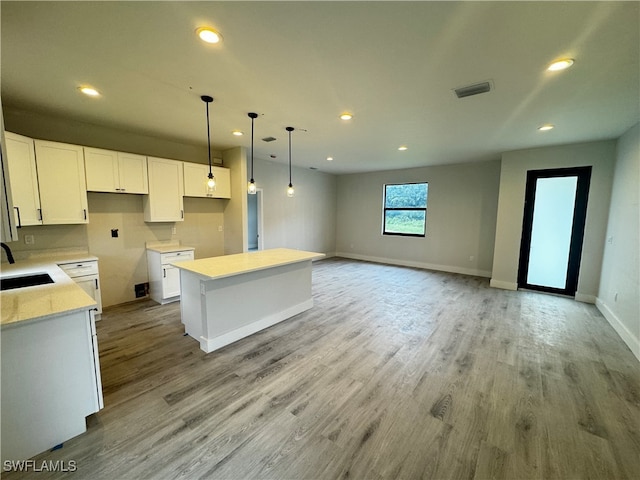 kitchen featuring light wood-type flooring, sink, decorative light fixtures, a center island, and white cabinetry