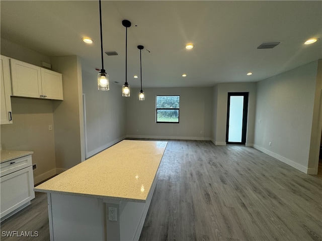 kitchen with a center island, hanging light fixtures, light stone countertops, light wood-type flooring, and white cabinetry