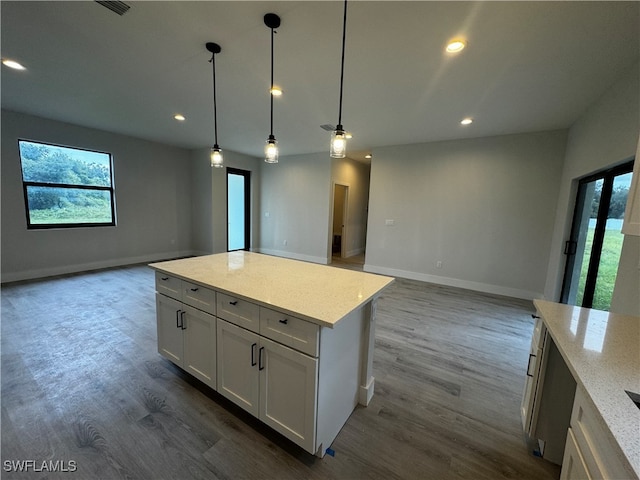 kitchen with a center island, white cabinets, light stone countertops, decorative light fixtures, and wood-type flooring