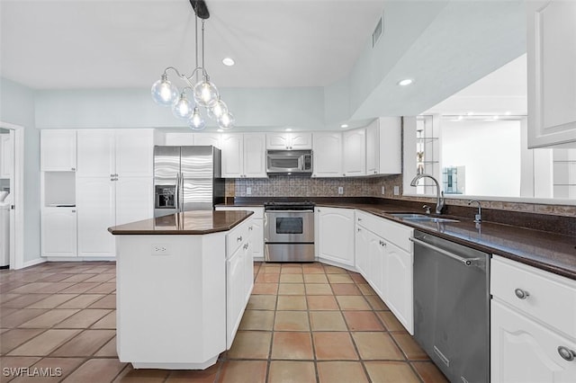 kitchen with white cabinets, appliances with stainless steel finishes, backsplash, a center island, and dark countertops