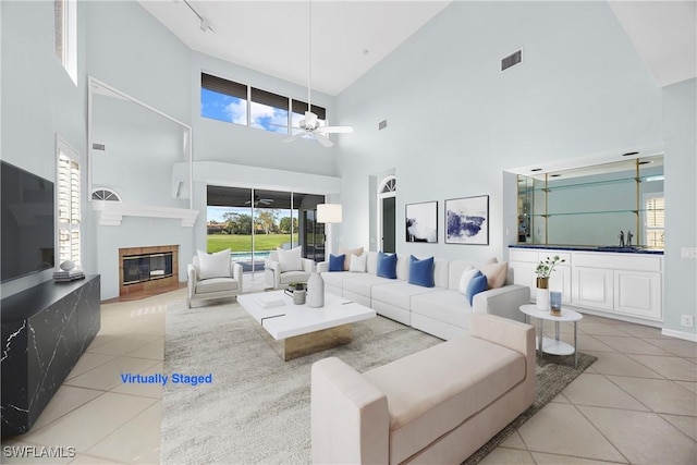 tiled living room with ceiling fan, sink, and a high ceiling