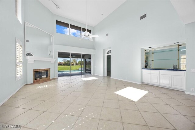 unfurnished living room with ceiling fan, light tile patterned floors, a towering ceiling, and sink