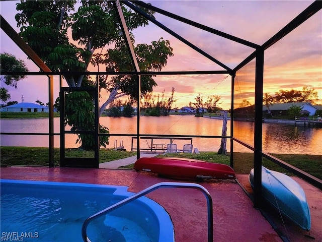 pool at dusk with a patio, a water view, and glass enclosure