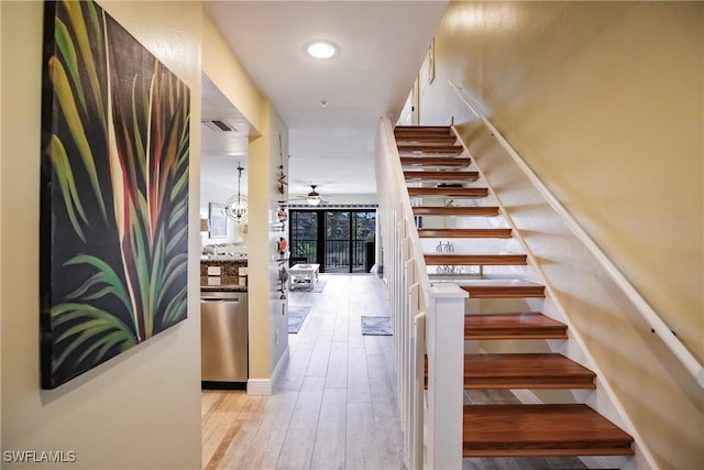 stairway with wood-type flooring and ceiling fan with notable chandelier