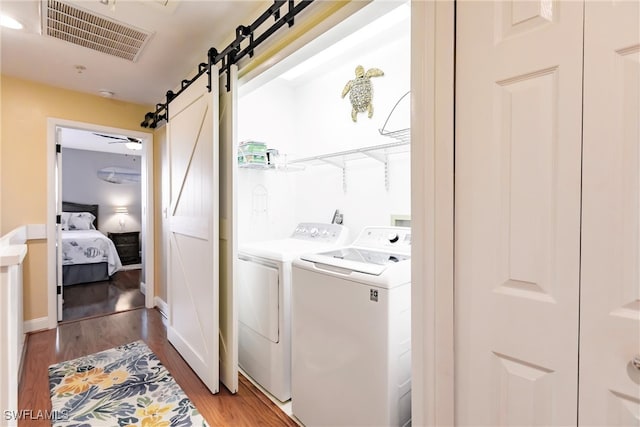 clothes washing area featuring a barn door, wood-type flooring, washing machine and dryer, and ceiling fan