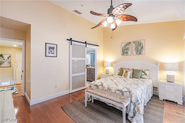 bedroom featuring ceiling fan, a barn door, wood-type flooring, vaulted ceiling, and ensuite bathroom