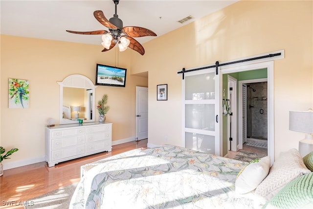 bedroom with ensuite bath, hardwood / wood-style flooring, a barn door, and ceiling fan