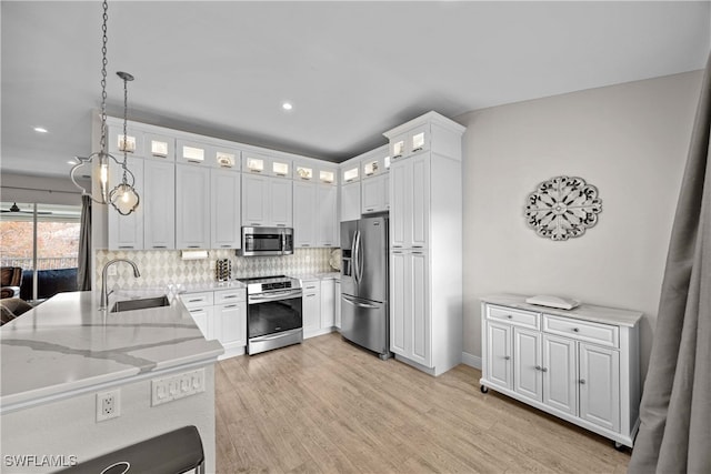 kitchen with appliances with stainless steel finishes, sink, hanging light fixtures, light hardwood / wood-style floors, and white cabinets