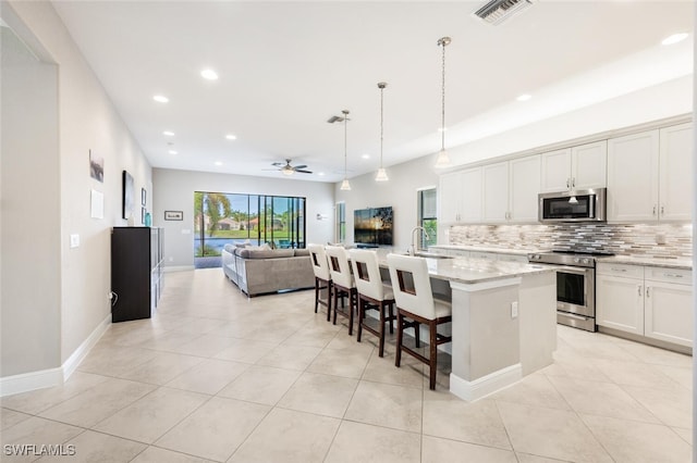 kitchen with white cabinetry, hanging light fixtures, a center island with sink, stainless steel appliances, and light stone countertops