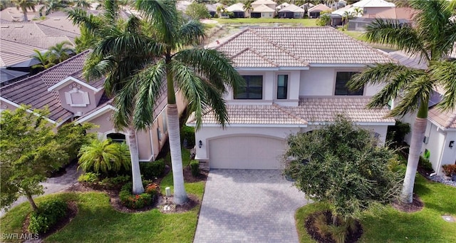 view of front of home with decorative driveway, a tiled roof, an attached garage, and stucco siding