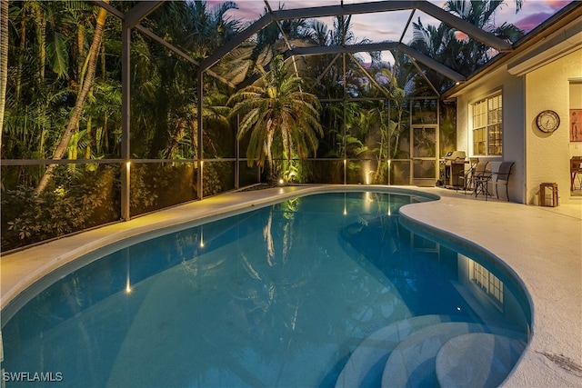 pool at dusk with a patio, area for grilling, and glass enclosure