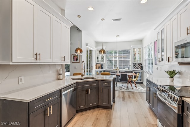 kitchen featuring light hardwood / wood-style flooring, sink, white cabinets, decorative light fixtures, and appliances with stainless steel finishes