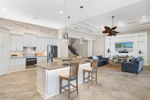 kitchen featuring a raised ceiling, light stone counters, a breakfast bar, white cabinets, and appliances with stainless steel finishes