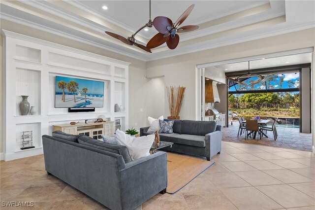 living area with built in features, a sunroom, ceiling fan, a tray ceiling, and crown molding