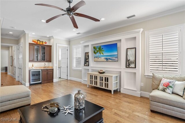 living room featuring sink, light wood-type flooring, crown molding, and beverage cooler