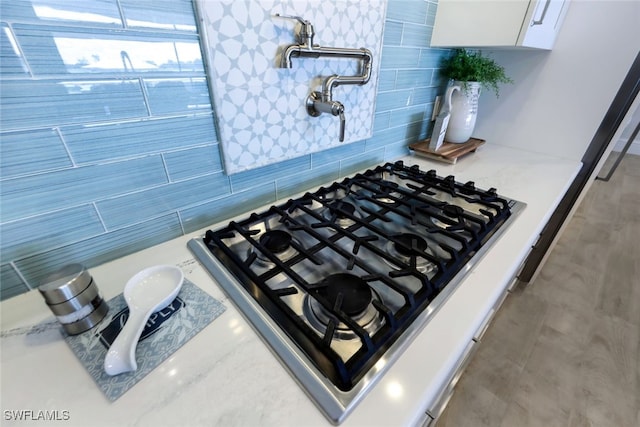 detailed view of pot filler, backsplash, white cabinetry, light stone countertops, and stainless steel gas stovetop