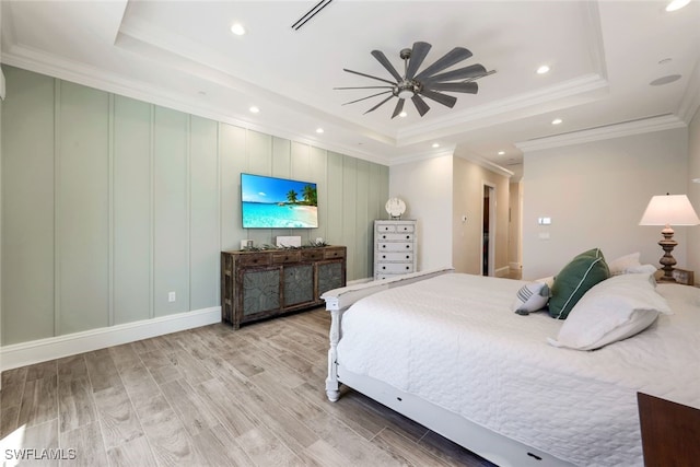 bedroom featuring a tray ceiling, wood finished floors, recessed lighting, a decorative wall, and crown molding