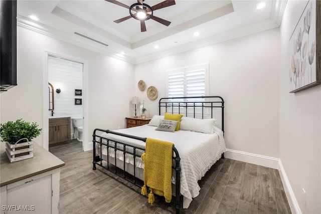 bedroom featuring a raised ceiling, wood finished floors, recessed lighting, crown molding, and connected bathroom