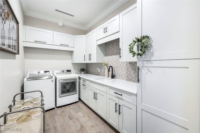 clothes washing area featuring washing machine and dryer, cabinet space, crown molding, and light wood-style flooring