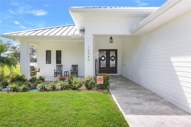 doorway to property featuring a standing seam roof, french doors, a lawn, a porch, and metal roof