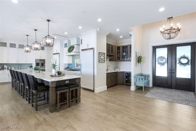 kitchen with a chandelier, built in refrigerator, beverage cooler, light countertops, and light wood finished floors