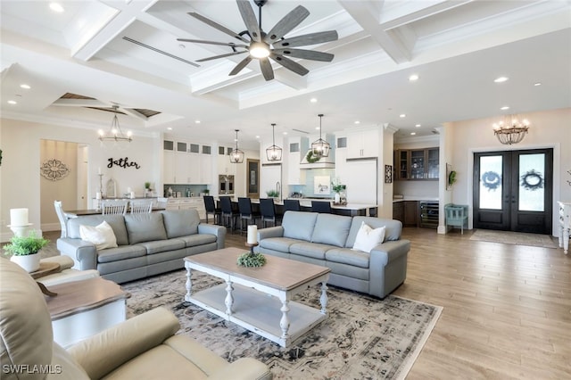 living room featuring coffered ceiling, beam ceiling, light hardwood / wood-style flooring, ornamental molding, and ceiling fan with notable chandelier