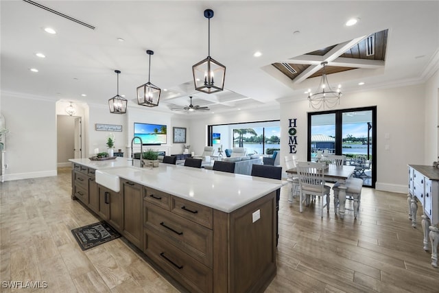 kitchen featuring light hardwood / wood-style flooring, coffered ceiling, sink, and a kitchen island with sink