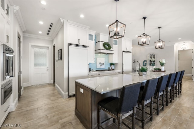 kitchen featuring a breakfast bar area, stainless steel appliances, a large island, decorative light fixtures, and white cabinets