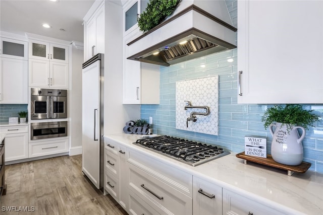 kitchen with decorative backsplash, appliances with stainless steel finishes, white cabinetry, light stone countertops, and light wood-type flooring