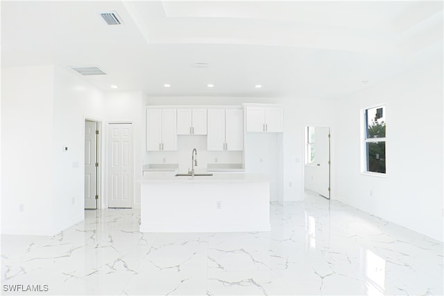 interior space with white cabinets, sink, and a kitchen island with sink