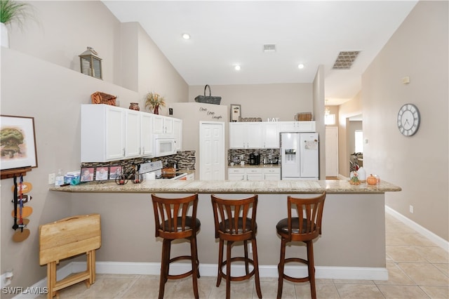 kitchen with decorative backsplash, kitchen peninsula, white appliances, and a breakfast bar